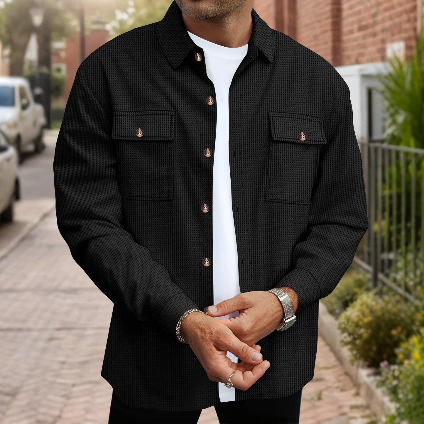 Man wearing black textured button-up shirt over white t-shirt standing on a city sidewalk