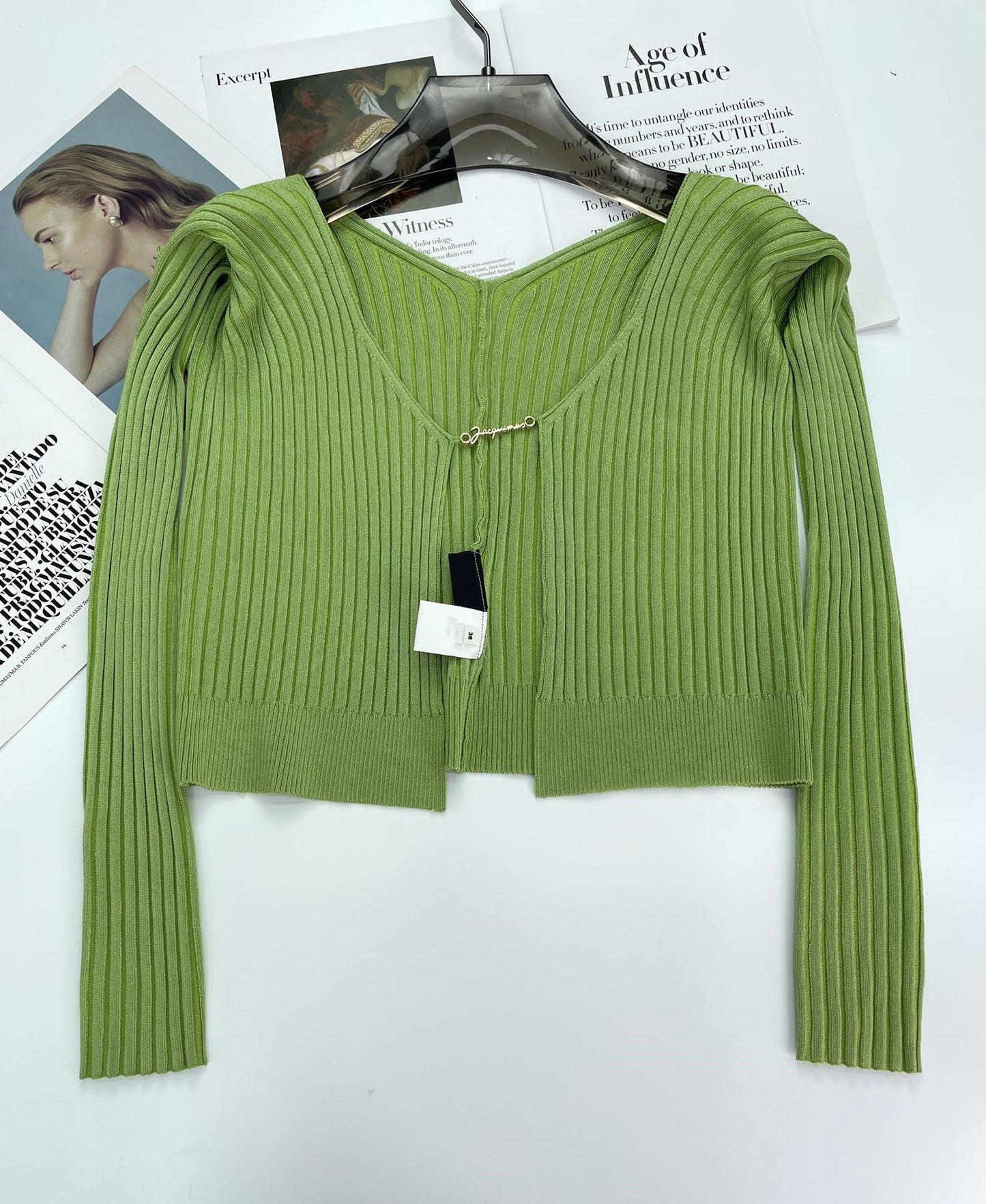 Green ribbed knit cardigan with V-neck on black hanger over fashion magazine pages