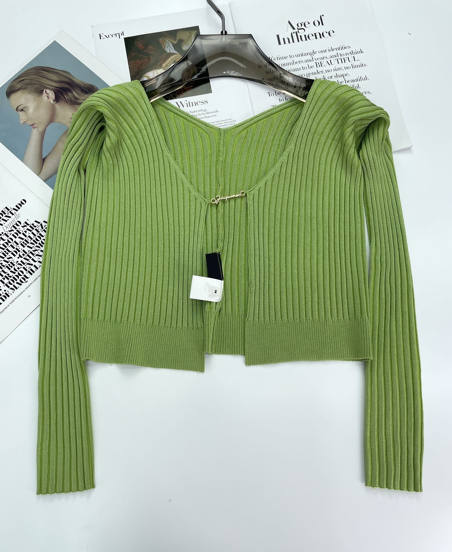 Green ribbed knit cardigan with V-neck on black hanger over fashion magazine pages