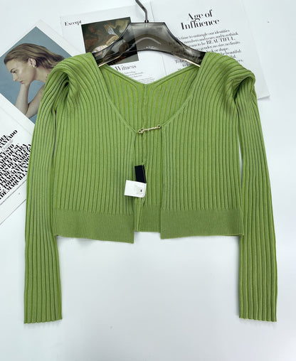 Green ribbed knit cardigan with V-neck on black hanger over fashion magazine pages