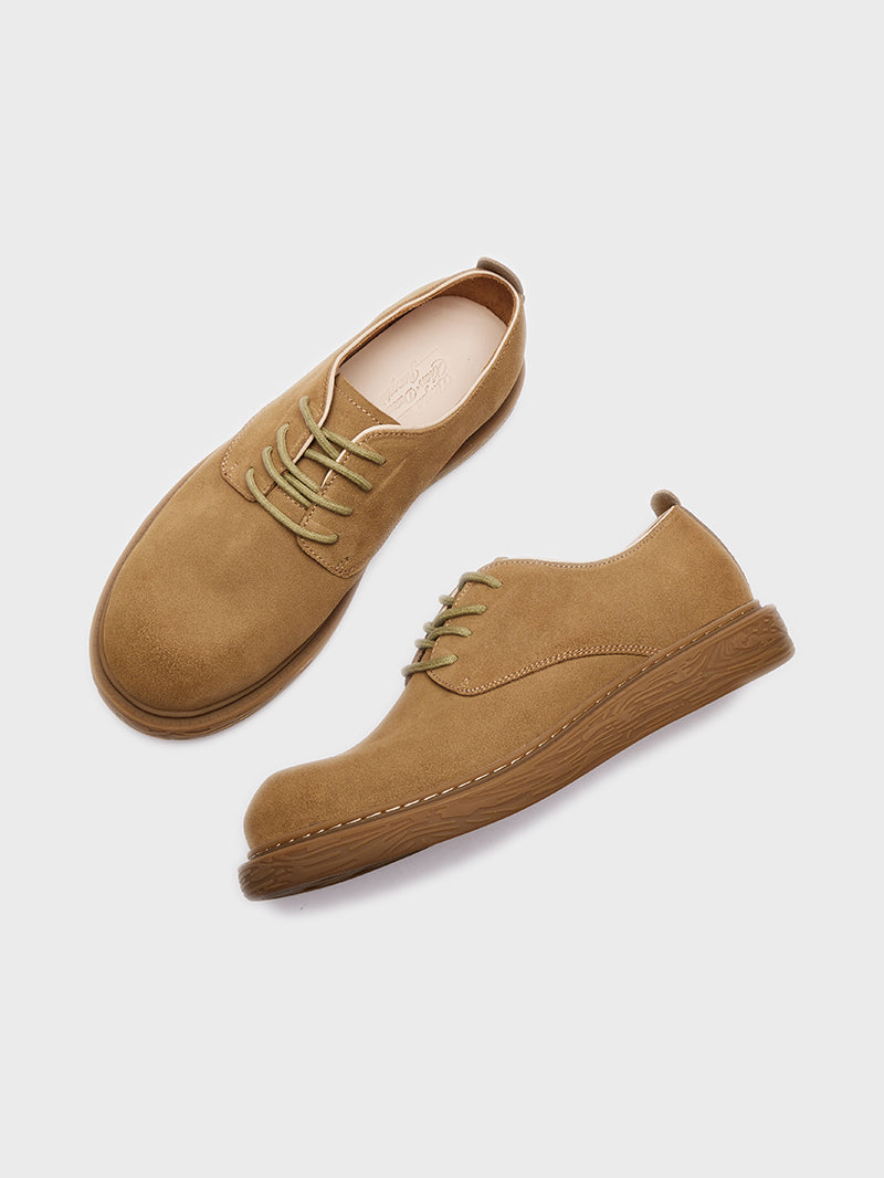 Pair of tan suede men's casual lace-up shoes with textured brown rubber soles on gray background
