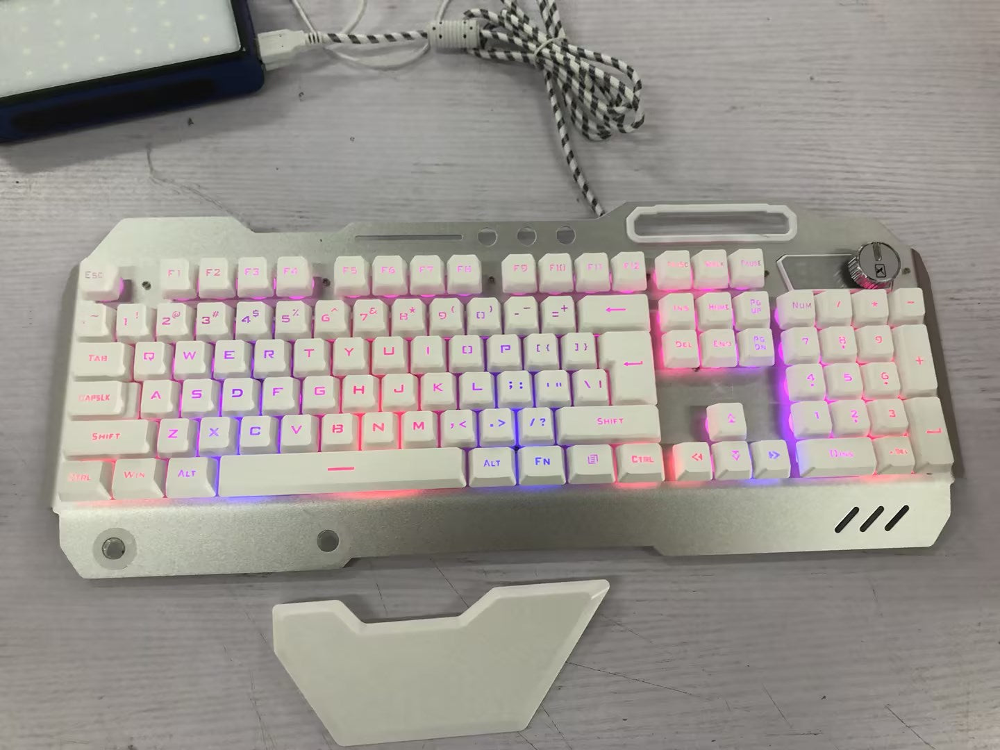 White mechanical gaming keyboard with multicolor LED backlight and volume control knob on gray wooden desk