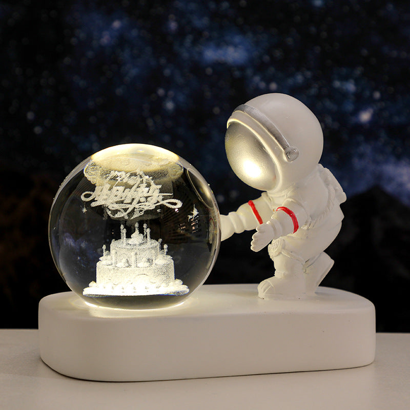 White astronaut figurine beside illuminated glass globe with a 3D birthday cake inside against a starry night background