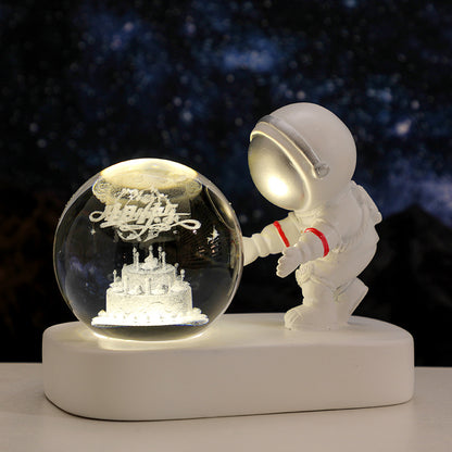 White astronaut figurine beside illuminated glass globe with a 3D birthday cake inside against a starry night background