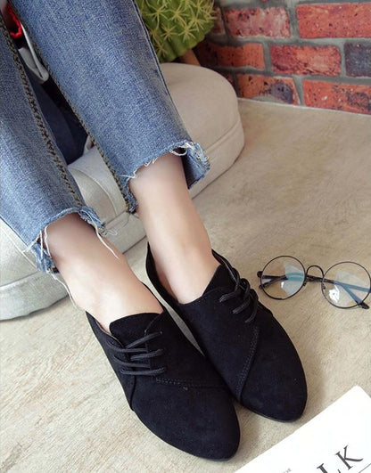Person wearing black suede lace-up pointed flats with frayed hem blue jeans sitting indoors