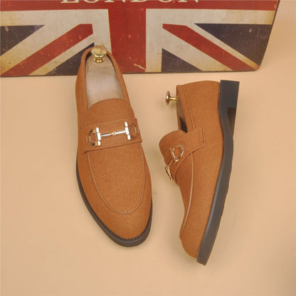 Pair of stylish brown suede loafers with gold horsebit detail and black rubber soles on beige background