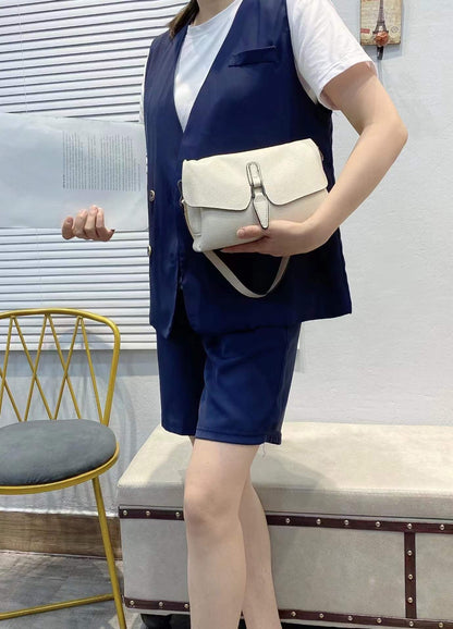 Person in navy vest and shorts holding beige leather handbag and white document in casual indoor setting