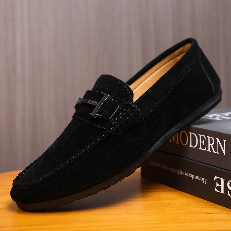 Black suede men's loafer with metal buckle detail on wooden surface near books