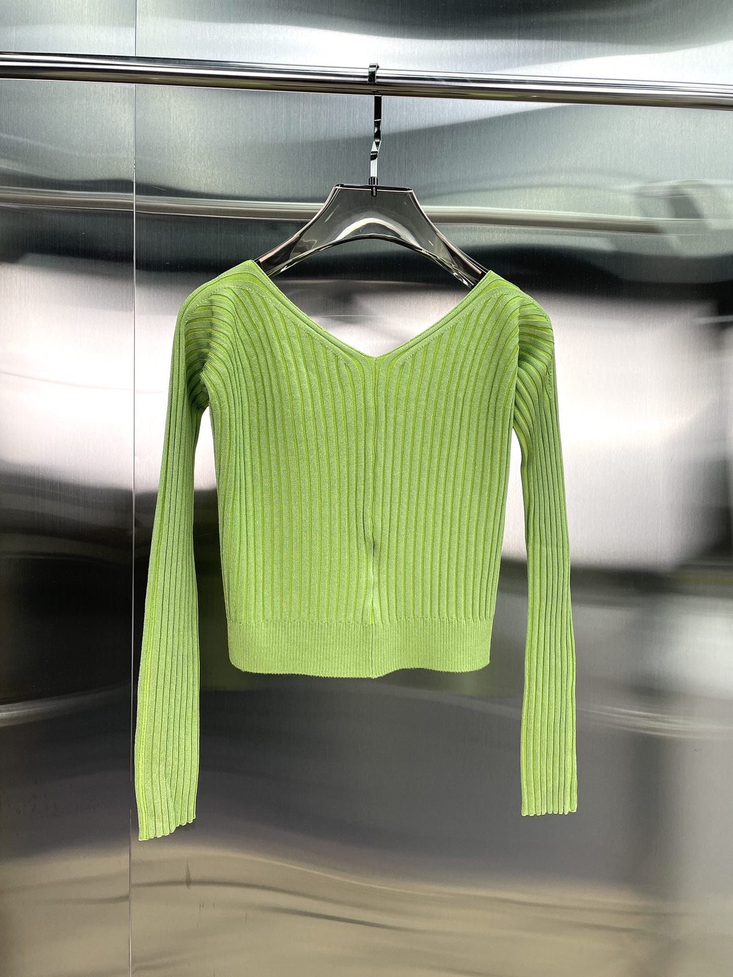 Light green ribbed knit long-sleeve cropped sweater hanging on a black hanger against a metallic background