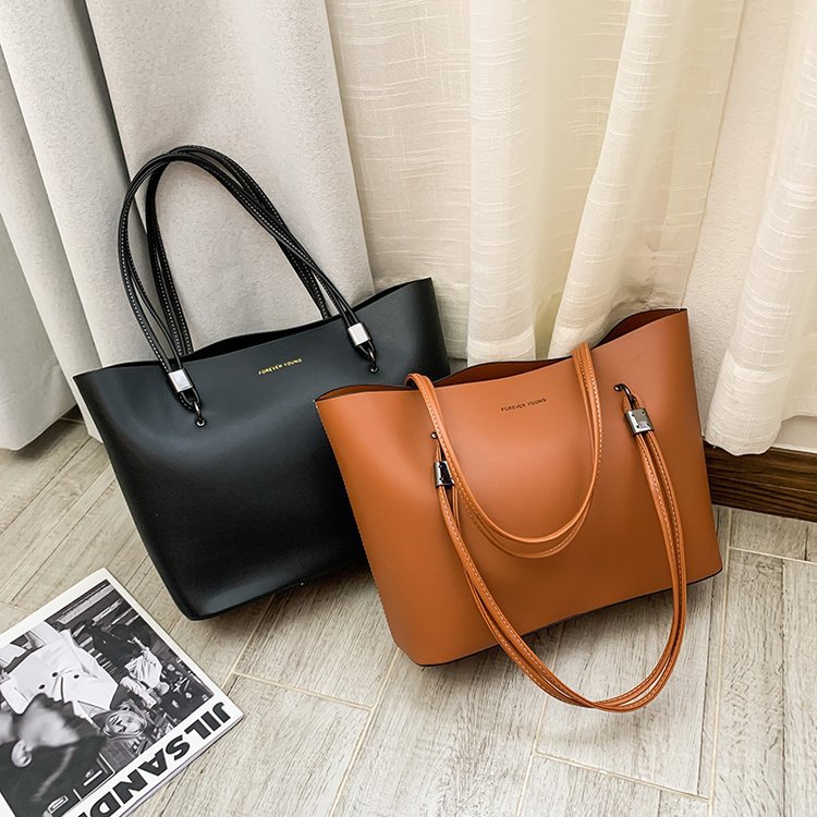 Black and brown leather tote bags with double handles placed on wooden floor near curtains