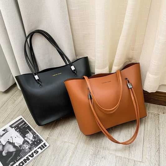 Black and brown leather tote bags with double handles placed on wooden floor near curtains