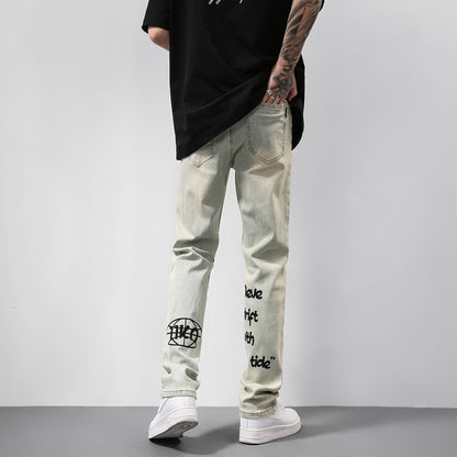Back view of person wearing light denim jeans with black graphic text and white sneakers against gray wall
