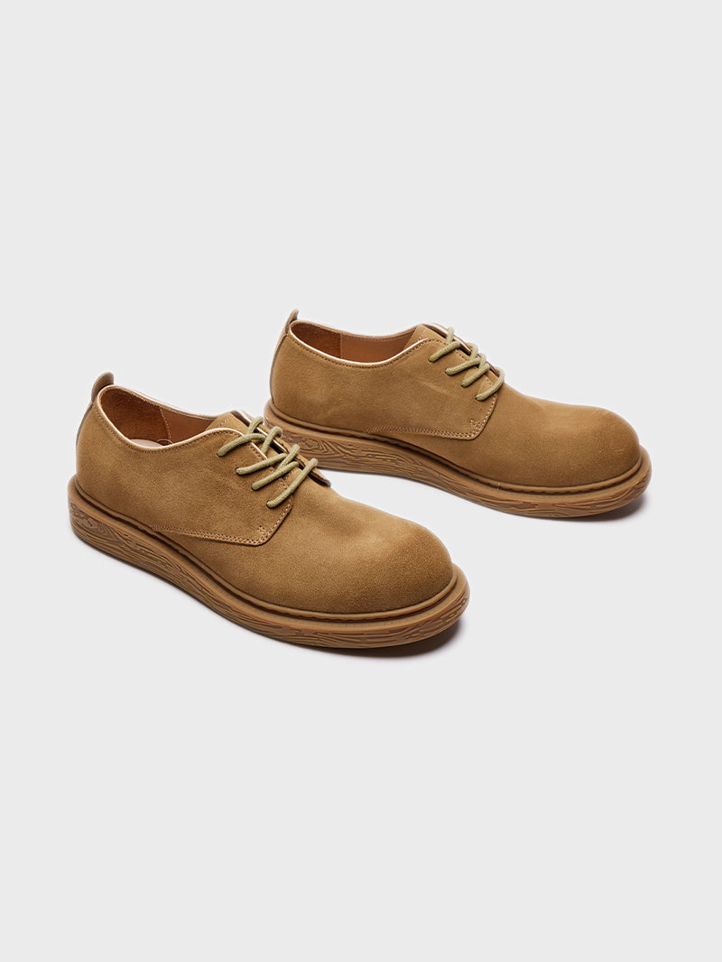 Pair of tan suede casual lace-up shoes with textured brown soles on gray background