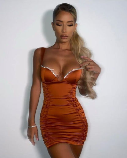 Woman wearing a tight orange satin mini dress with rhinestone trim, posing against white background