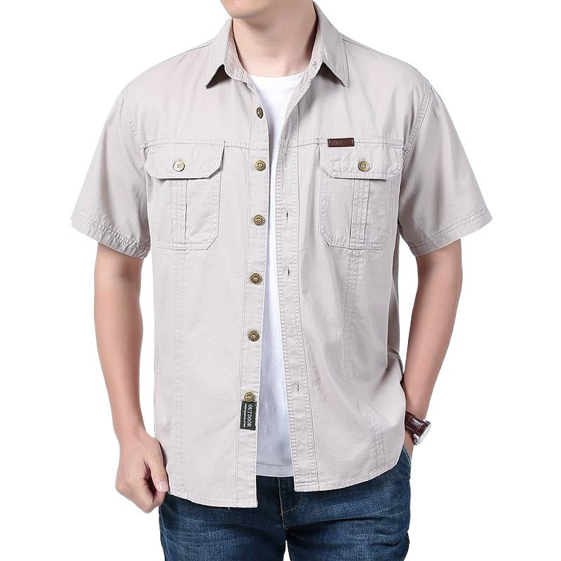 Man wearing beige short-sleeve button-up shirt with two chest pockets over white t-shirt and blue jeans