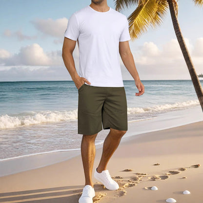 Man wearing white t-shirt, olive green shorts, and white sneakers on a tropical beach with palm tree