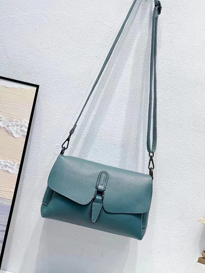 Blue leather crossbody bag with flap and buckle hanging on white textured wall