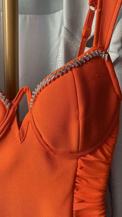 Close-up of orange dress with rhinestone strap embellishments hanging near white garment