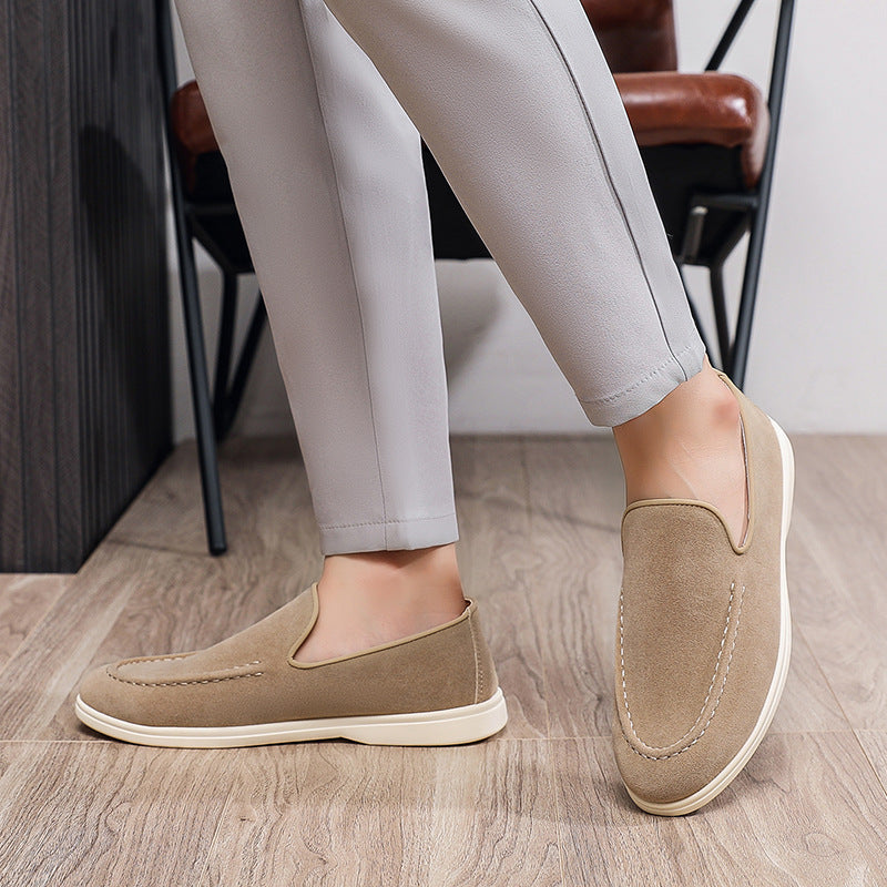 Close-up of beige suede loafers with white soles worn with gray pants on wood floor