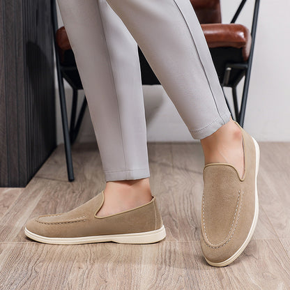 Close-up of beige suede loafers with white soles worn with gray pants on wood floor