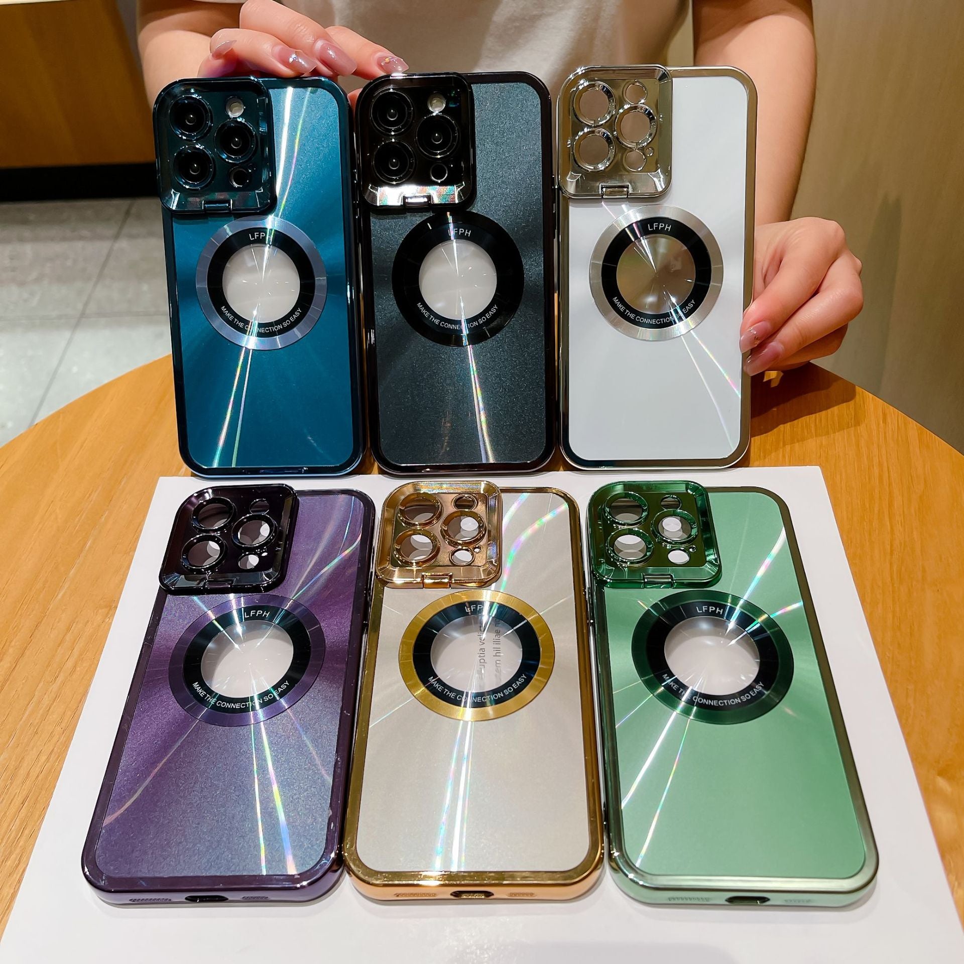 Six colorful magnetic phone cases with camera lens protectors displayed on table, held by hands