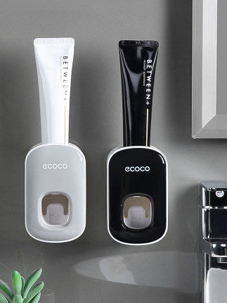 Wall-mounted Ecoco toothpaste dispensers holding black and white Between+ toothpaste tubes in bathroom