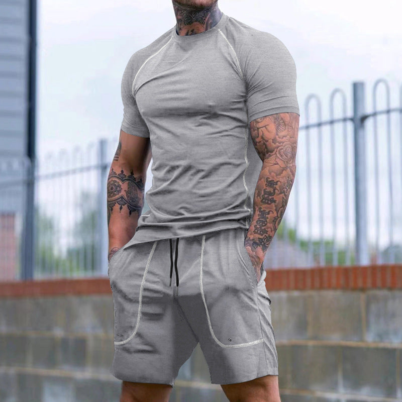 muscular man with tattooed arms wearing fitted grey short sleeve t-shirt and matching shorts outdoors
