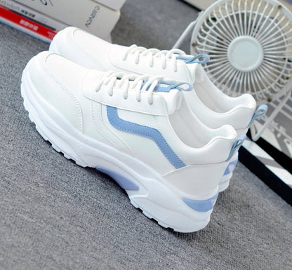 White chunky sneakers with blue accents and thick soles on gray carpet, styled casual shoes