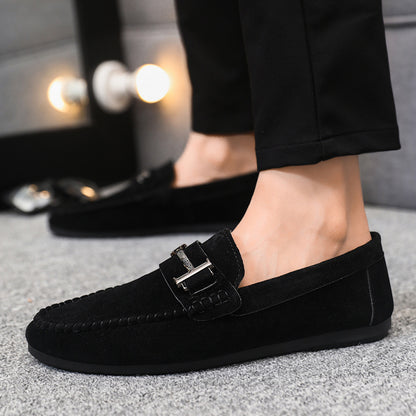Black suede men's loafers with metal buckle detail worn with black pants on gray carpet