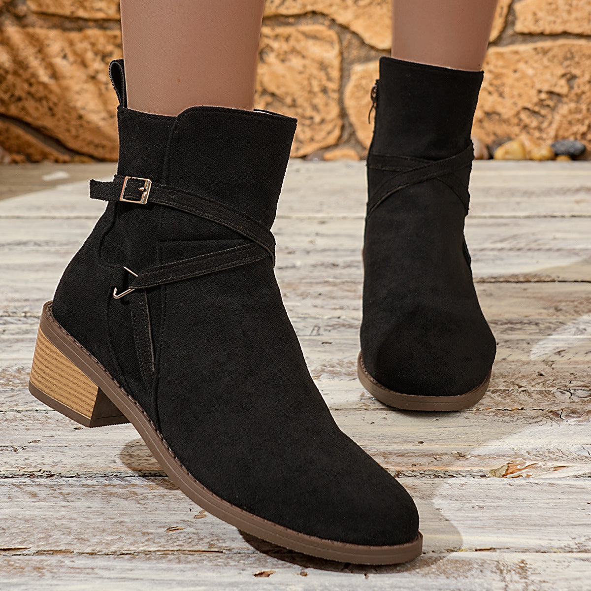 Black suede ankle boots with wooden block heels and buckle straps on wooden floor