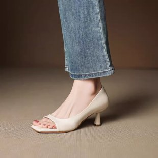 Close-up of foot wearing beige open-toe kitten heel shoe with blue jeans on neutral background