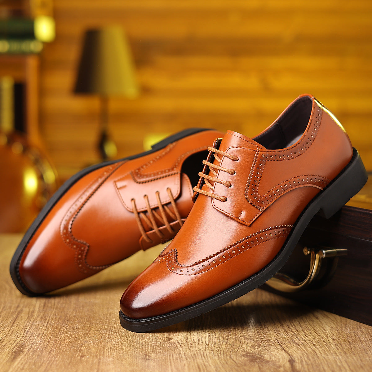 Pair of polished brown leather dress shoes with brogue detailing on wooden surface