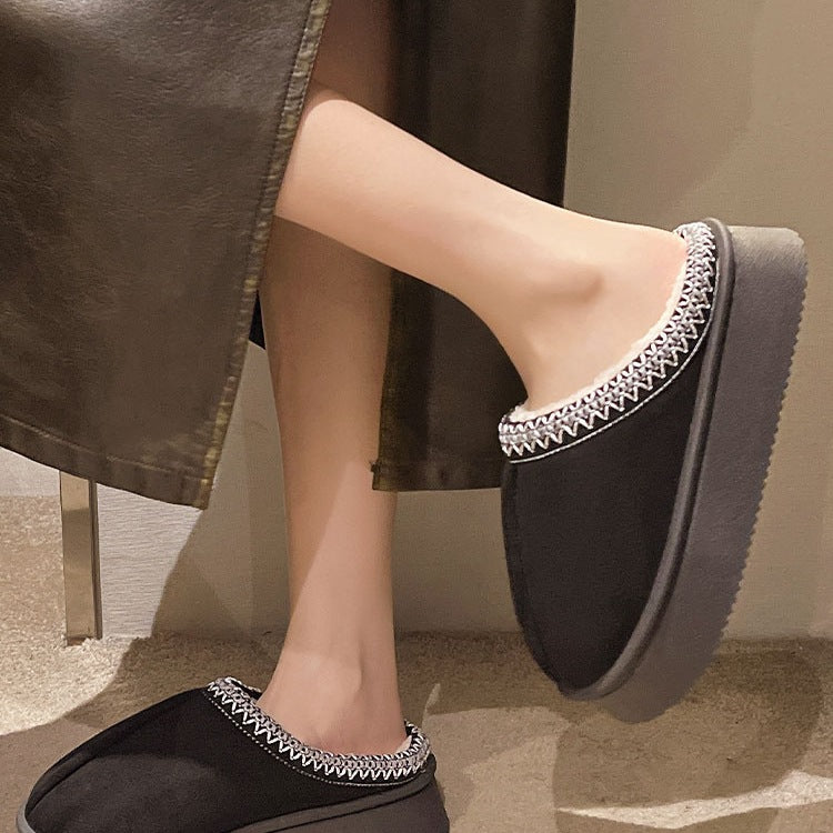 Person wearing black slip-on platform slippers with white embroidered trim indoors
