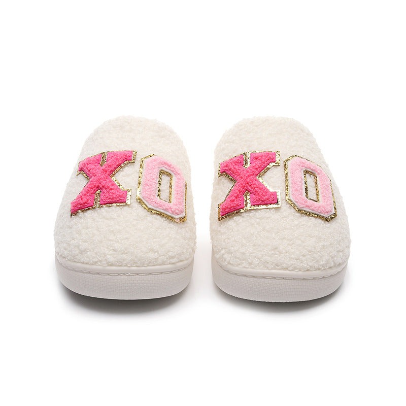 White fuzzy slippers with pink and gold XO letters on top, cozy indoor footwear