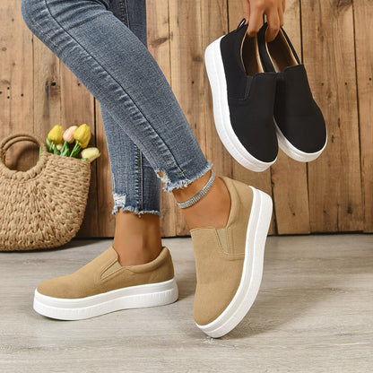 Person wearing beige slip-on sneakers with white soles and holding black slip-on sneakers indoors