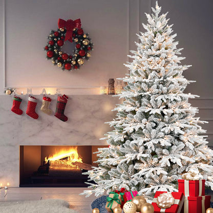 Flocked Christmas tree with lights and gifts by a lit fireplace with stockings and holiday wreath