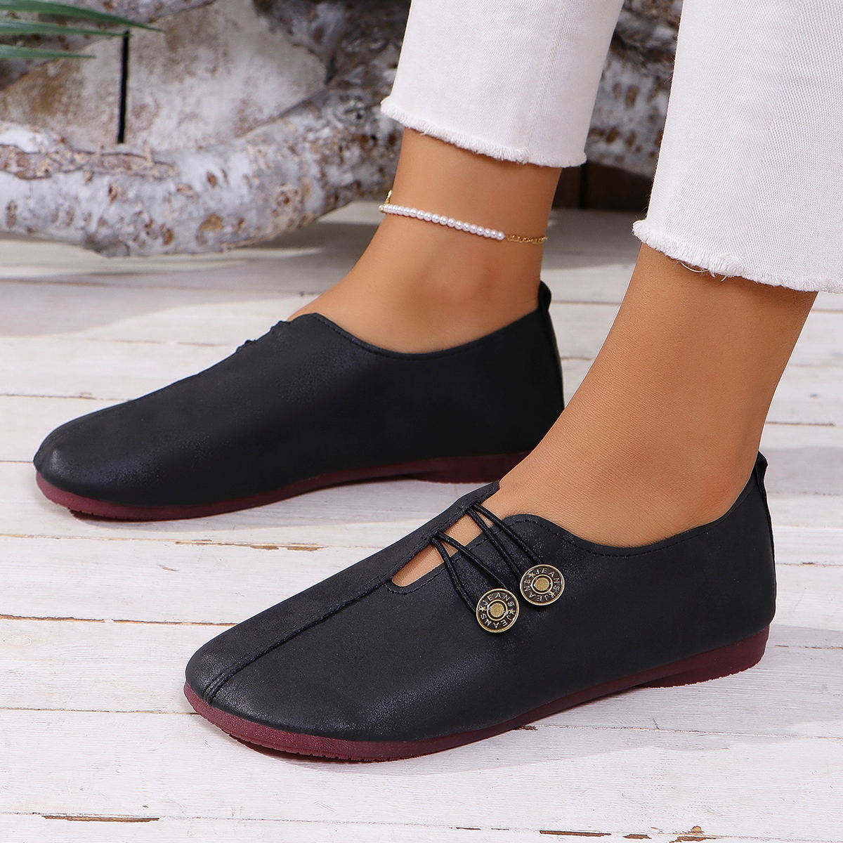 Close-up of black casual slip-on shoes with decorative buttons on female feet wearing white frayed jeans