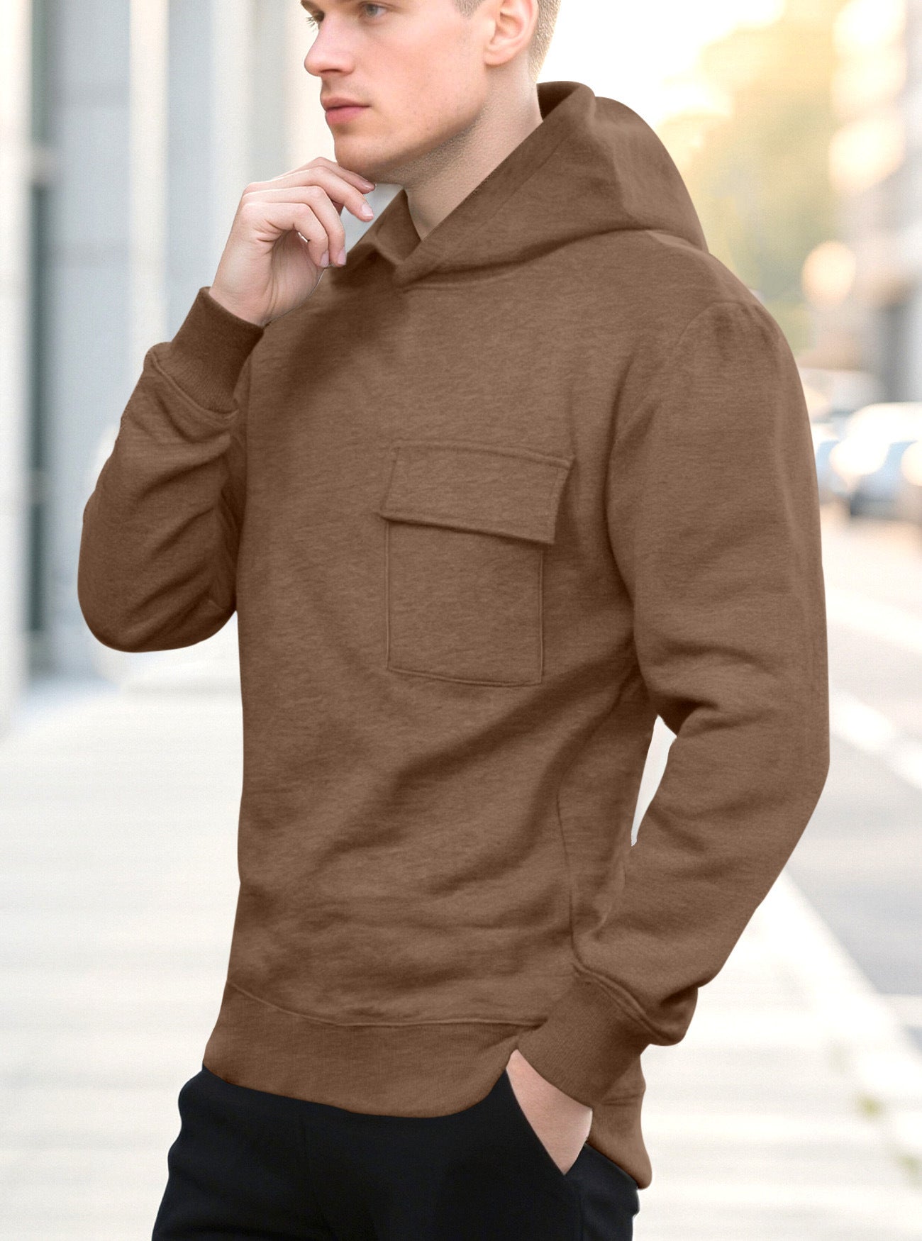 Man wearing brown hoodie with front pocket standing outdoors on city sidewalk