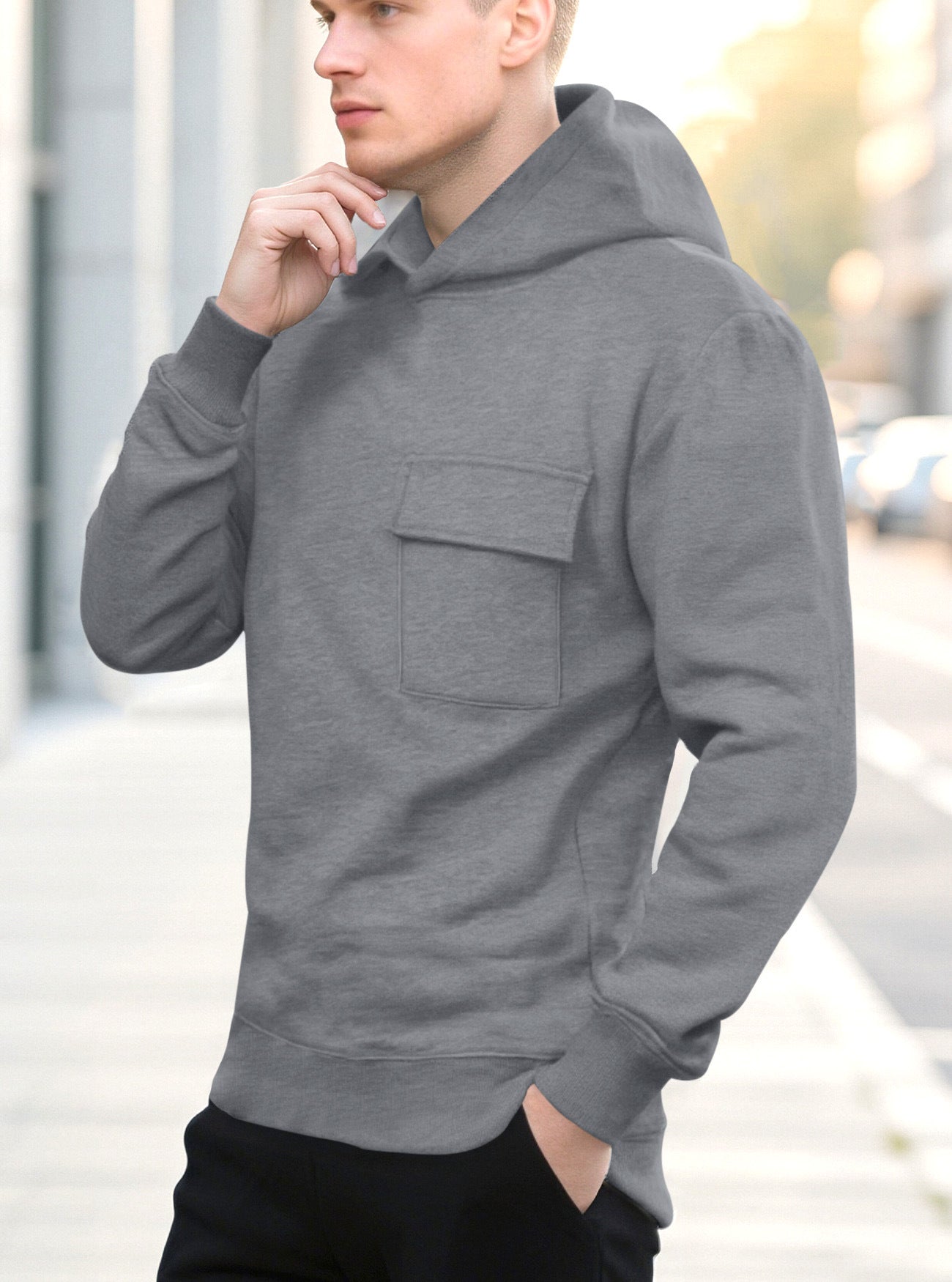Young man wearing a gray hoodie with a front pocket standing outdoors on a city street