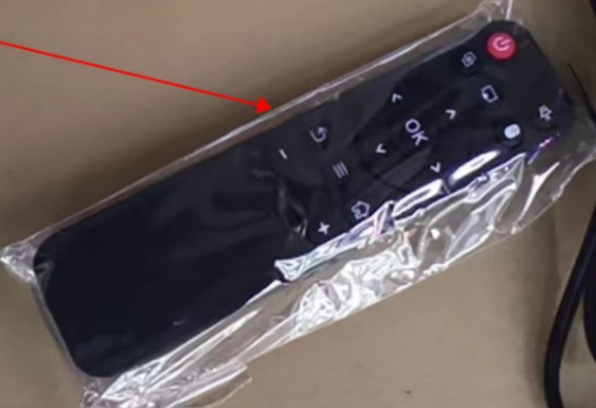Black TV remote control with red power button in clear plastic packaging on cardboard surface