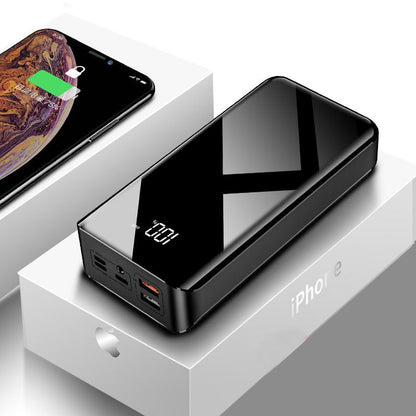 Black glossy portable power bank with digital display on iPhone packaging box, smartphone charging nearby