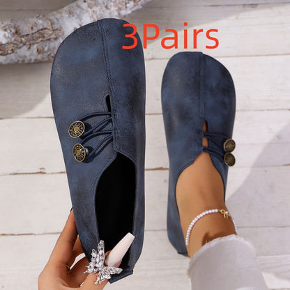 Pair of navy blue minimalist slip-on flat shoes with decorative buttons, worn on wooden floor