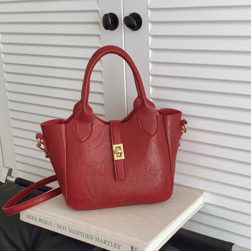 Red leather handbag with gold clasp on white book near white shutter doors