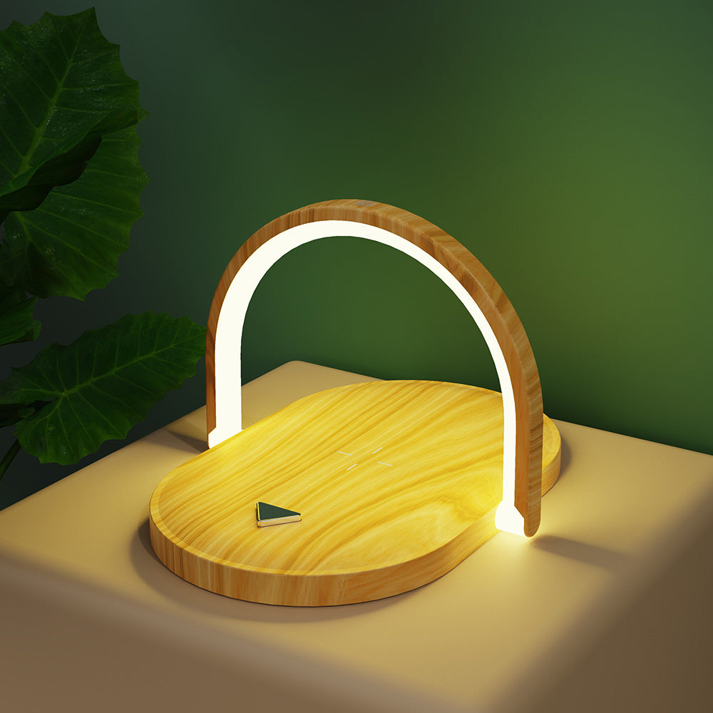 Modern wooden LED lamp with curved light frame on beige table near green wall and plant