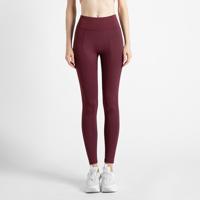 Front view of woman wearing high-waisted burgundy leggings with white sneakers on white background