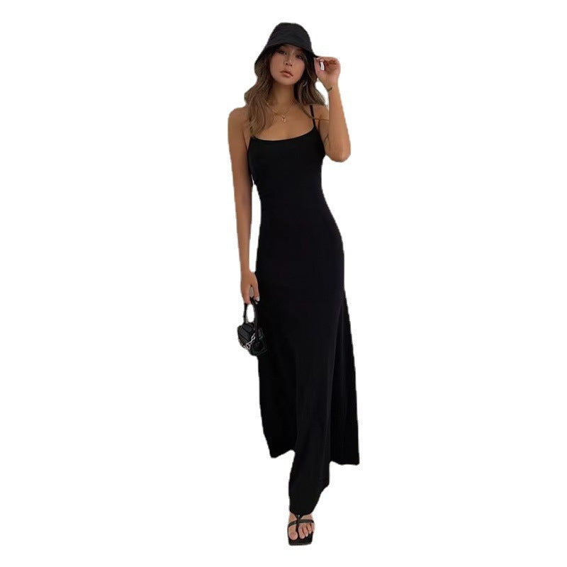 Woman wearing a black spaghetti strap maxi dress with black bucket hat and sandals carrying a small black handbag