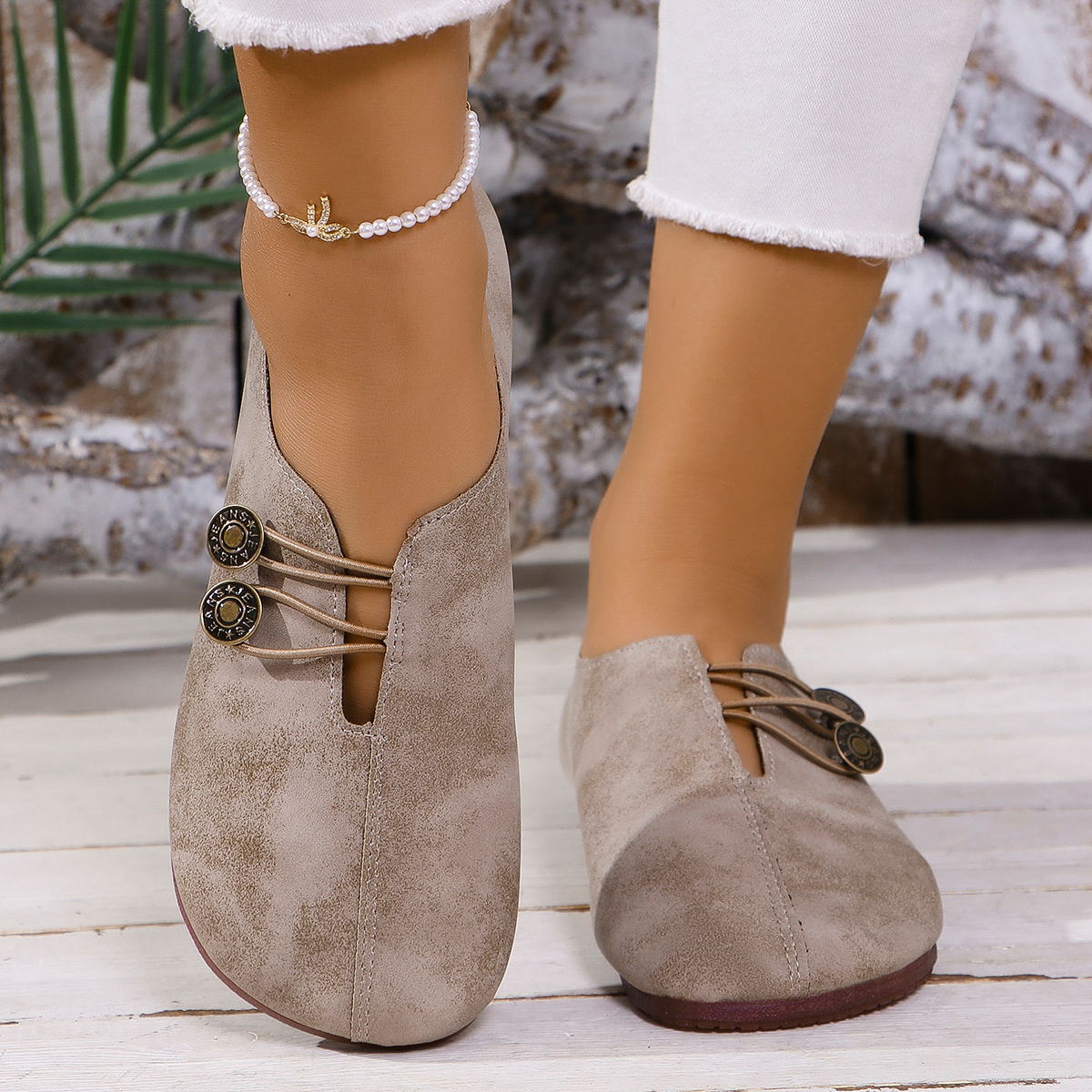 Close-up of feet wearing taupe suede slip-on shoes with button details and white cropped jeans