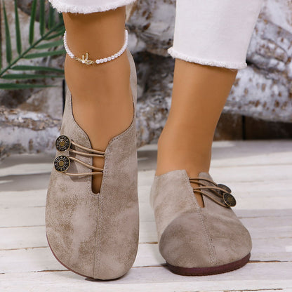 Close-up of feet wearing taupe suede slip-on shoes with button details and white cropped jeans