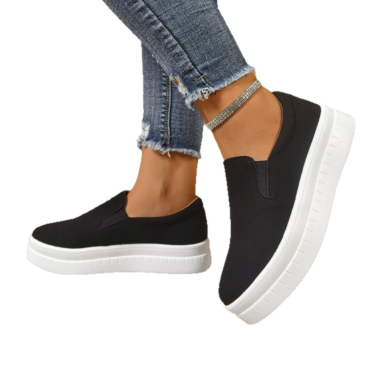 Black slip-on platform sneakers with white soles worn with frayed blue jeans and rhinestone ankle bracelet