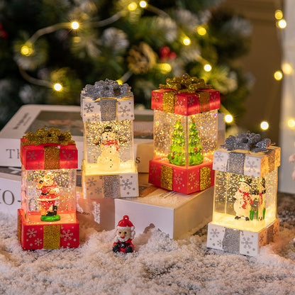 Illuminated Christmas gift box decorations with Santa, snowman, and tree inside, surrounded by artificial snow